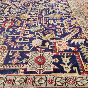 May include: A rectangular area rug featuring a deep blue field with an intricate pattern of floral motifs, geometric shapes, and scrolling vines in shades of red, cream, yellow, and green, finished with a wide border in soft pink and light green.