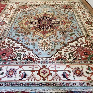 May include: A large, intricately patterned rug with a light blue center and a white border. The rug features a variety of colors, including red, green, and yellow. The rug is made of wool and has a traditional design.