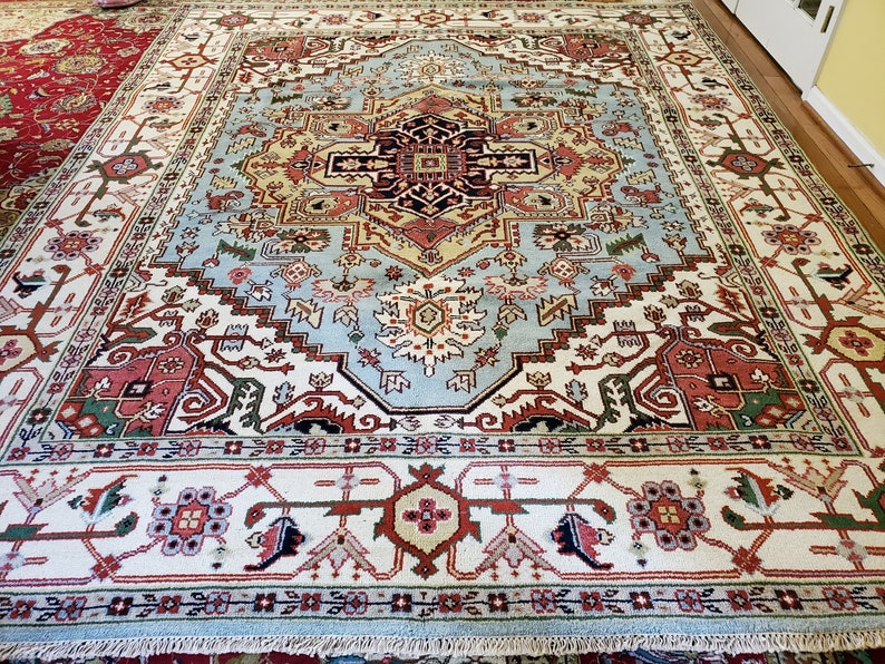 May include: A large, intricately patterned rug with a light blue center and a white border. The rug features a variety of colors, including red, green, and yellow. The rug is made of wool and has a traditional design.