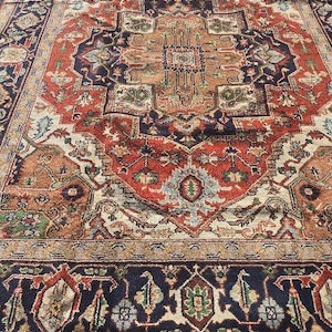 Puede incluir: Una alfombra persa tradicional con un diseño detallado e intrincado. La alfombra presenta un medallón central con un patrón repetitivo de motivos florales y formas geométricas. Los colores son ricos y vibrantes, incluyendo tonos de rojo, azul, beige y marfil.