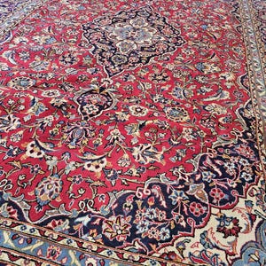 May include: A large, ornate red rug with a detailed floral pattern. The rug features a central medallion and borders in navy blue, cream, and light blue. The intricate design includes various floral and leaf motifs.