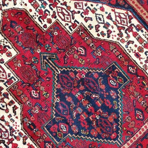 Op de afbeelding: Een close-up van een rood, blauw en wit gepatroneerd tapijt met ingewikkelde ontwerpen. Het tapijt heeft een traditionele Perzische stijl.
