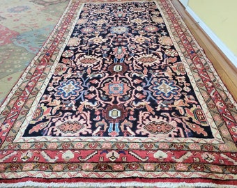 Può includere: Un tappeto persiano tradizionale con sfondo blu scuro e intricati motivi floreali in tonalità di rosso, rosa, blu e beige. Il tappeto ha un bordo largo con un motivo geometrico ripetitivo.