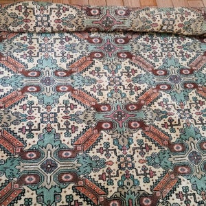 Puede incluir: Una alfombra vintage con un patrón geométrico en tonos marrones, verde azulado, rosa y crema. La alfombra tiene un diseño tradicional con detalles intrincados.