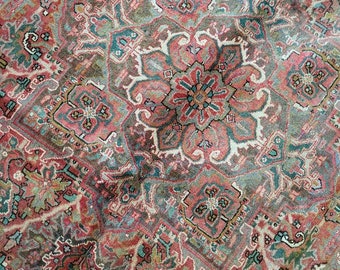 Op de afbeelding: Een vintage Perzisch tapijt met een gedetailleerd geometrisch patroon in tinten rood, roze, groen en blauw.