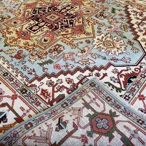 May include: A close-up of a traditional rug with intricate patterns in shades of red, blue, green, and white. The rug has a detailed border and a central medallion.