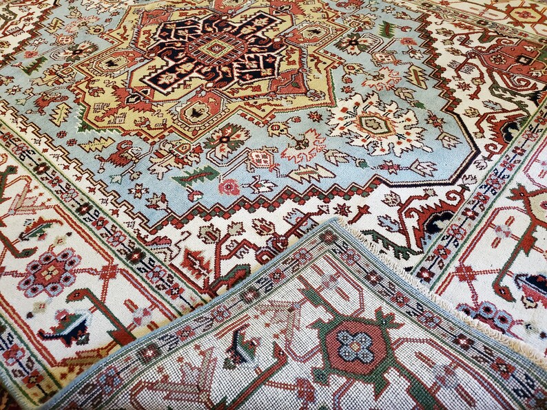 May include: A close-up of a traditional rug with intricate patterns in shades of red, blue, green, and white. The rug has a detailed border and a central medallion.