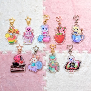 Op de afbeelding: Negen kleurrijke sleutelhangers met verschillende dierenpersonages uit de Animal Crossing-videogameserie. Elke sleutelhanger is gemaakt van helder acryl en heeft een ander personage, waaronder een eekhoorn, een hond, een kikker, een konijn en een pinguïn. De sleutelhangers zijn allemaal bevestigd aan gouden metalen ringen.