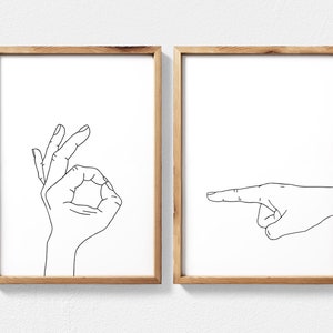 Puede incluir: Dos impresiones enmarcadas con dibujos de l&iacute;neas negras de manos haciendo gestos. La impresi&oacute;n de la izquierda muestra una mano haciendo el signo de OK. La impresi&oacute;n de la derecha muestra una mano apuntando hacia la derecha.