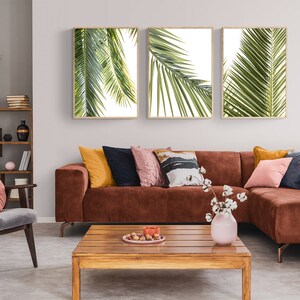May include: A brown sectional sofa with a variety of throw pillows in a living room setting. The sofa is in front of a wall with three framed prints of palm leaves. A wooden coffee table sits in front of the sofa.