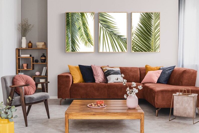 May include: A brown sectional sofa with a variety of throw pillows in a living room setting. The sofa is in front of a wall with three framed prints of palm leaves. A wooden coffee table sits in front of the sofa.