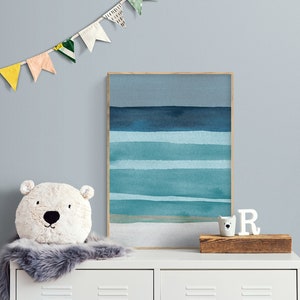 May include: A white dresser with two drawers, a fluffy white and gray rug, a white stuffed animal with a bear face, a framed watercolor painting of a blue and green ocean scene, and a white wooden letter 'R' on a wooden shelf.