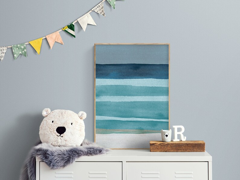 May include: A white dresser with two drawers, a fluffy white and gray rug, a white stuffed animal with a bear face, a framed watercolor painting of a blue and green ocean scene, and a white wooden letter 'R' on a wooden shelf.
