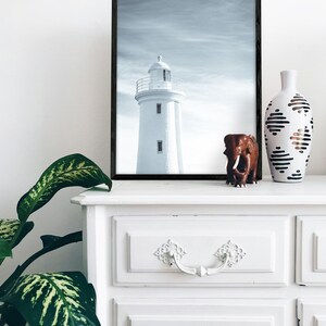 Pu&ograve; includere: Una fotografia in bianco e nero di un faro incorniciato da una cornice nera, una statuetta di elefante marrone e un vaso bianco con motivi geometrici neri e marroni su una cassettiera bianca con due cassetti.