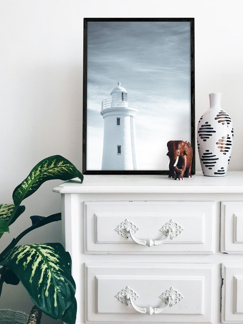 Pu&ograve; includere: Una fotografia in bianco e nero di un faro incorniciato da una cornice nera, una statuetta di elefante marrone e un vaso bianco con motivi geometrici neri e marroni su una cassettiera bianca con due cassetti.