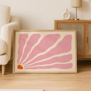 Peut inclure: Une affiche encadrée représentant une grande fleur abstraite. L'œuvre d'art présente une fleur rose clair avec un centre orange sur un fond crème. L'impression est encadrée dans un cadre en bois clair, idéale pour la décoration intérieure.