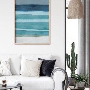 May include: A framed abstract watercolor painting with horizontal stripes in shades of blue and green. The painting is in a light wood frame and is hanging on a white wall.