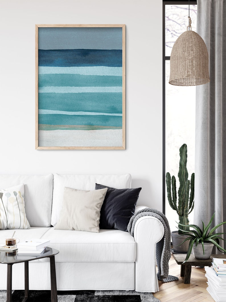 May include: A framed abstract watercolor painting with horizontal stripes in shades of blue and green. The painting is in a light wood frame and is hanging on a white wall.