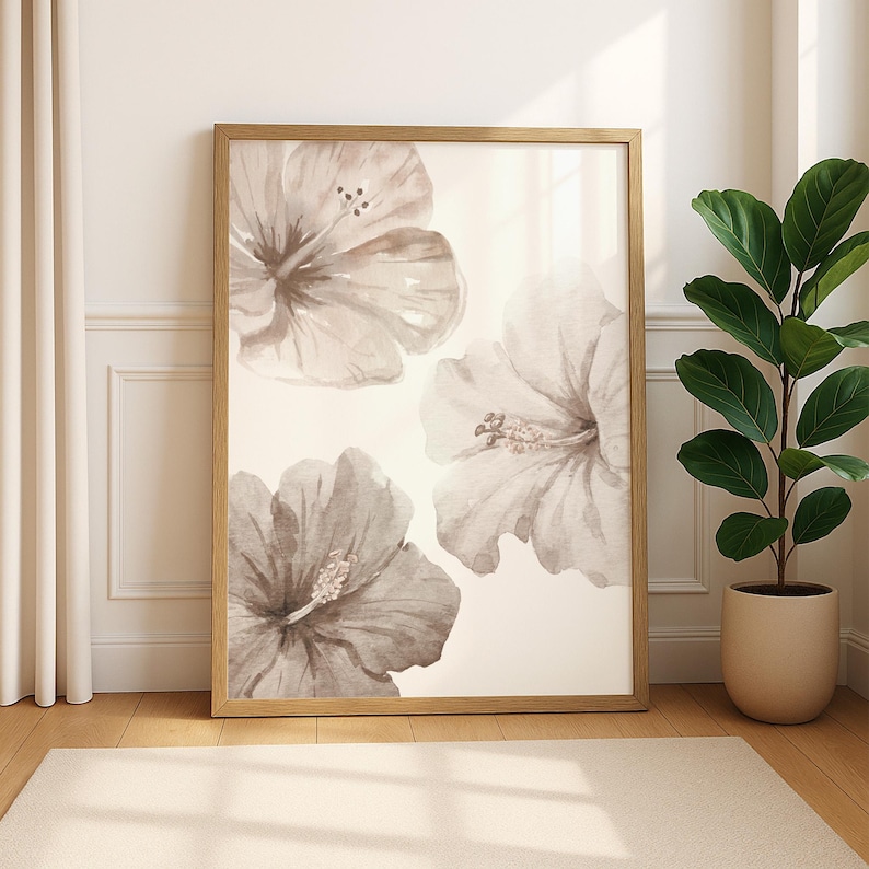 May include: A framed floral art print featuring three large hibiscus flowers in shades of gray and beige. The artwork is displayed in a light wood frame and leans against a white wall. A potted plant sits to the right.