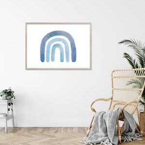 May include: A framed watercolor painting of a blue rainbow on a white background. The rainbow is made up of four arches, with the top arch being the darkest blue and the bottom arch being the lightest blue. The rainbow is centered in the frame.
