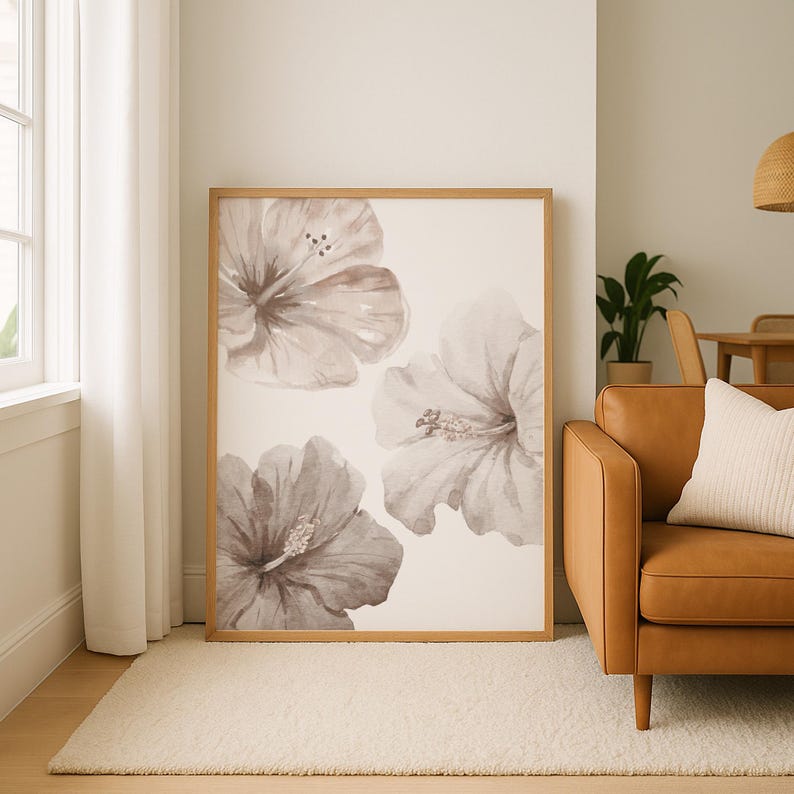 May include: A framed art print featuring three watercolor hibiscus flowers in shades of gray and brown. The artwork has a light background and is displayed in a natural wood frame. The print is leaning against a wall in a living room setting.