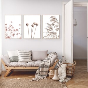 K&ouml;nnte beinhalten: Drei gerahmte botanische Drucke mit minimalistischer &Auml;sthetik. Die Drucke zeigen getrocknete Blumen und Gr&auml;ser in Braun- und Beiget&ouml;nen. Die Drucke h&auml;ngen an einer wei&szlig;en Wand &uuml;ber einem hellgrauen Sofa mit Holzrahmen.