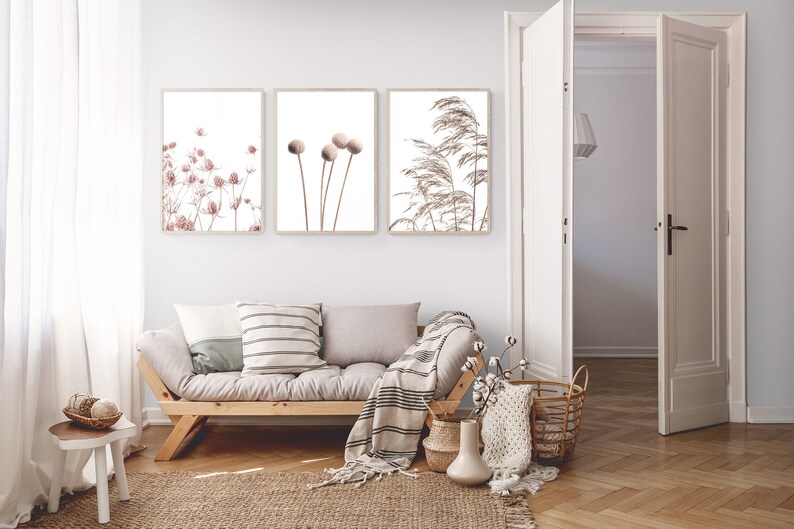 K&ouml;nnte beinhalten: Drei gerahmte botanische Drucke mit minimalistischer &Auml;sthetik. Die Drucke zeigen getrocknete Blumen und Gr&auml;ser in Braun- und Beiget&ouml;nen. Die Drucke h&auml;ngen an einer wei&szlig;en Wand &uuml;ber einem hellgrauen Sofa mit Holzrahmen.