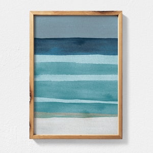 May include: A framed abstract watercolor painting with horizontal stripes in shades of blue and green. The painting depicts a seascape with a light blue sky and a sandy beach.