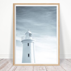 Pu&ograve; includere: Un faro bianco con una ringhiera nera si erge alto contro un cielo nuvoloso e blu. Il faro &egrave; un simbolo classico di speranza e guida.