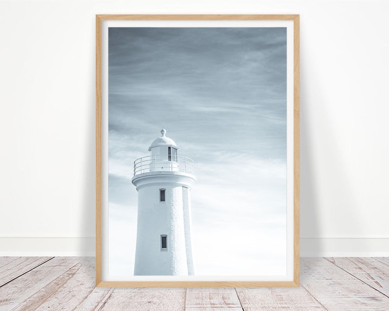 Pu&ograve; includere: Un faro bianco con una ringhiera nera si erge alto contro un cielo nuvoloso e blu. Il faro &egrave; un simbolo classico di speranza e guida.