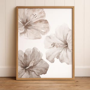 Neutral oversized hibiscus floral wall art print in warm beige tones, framed and styled in a beautiful coastal space. Featuring three subtle, oversized watercolor hibiscus blooms in earthy tones