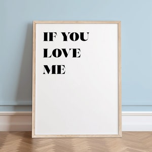 May include: A white framed poster with black text that reads "IF YOU LOVE ME". The poster is hanging on a light blue wall with white trim.