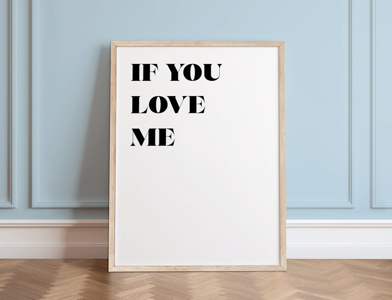 May include: A white framed poster with black text that reads "IF YOU LOVE ME". The poster is hanging on a light blue wall with white trim.