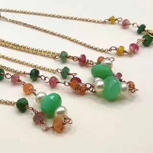 Op de afbeelding: Een ketting met meerdere strengen met gouden kettingen en een verscheidenheid aan kleurrijke kralen. De kralen zijn groen, roze, oranje en wit, waardoor een levendig accessoire ontstaat. De ketting is ontworpen met een delicaat en ingewikkeld patroon.