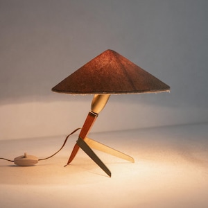 May include: A vintage table lamp with a brown conical shade. The base is made of wood, brass, and metal. The lamp has a cord with an on/off switch. The lamp is a decorative lighting fixture. The lamp's design is reminiscent of the mid-20th century.