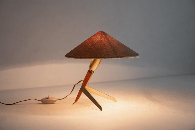 May include: A vintage table lamp with a brown conical shade. The base is made of wood, brass, and metal. The lamp has a cord with an on/off switch. The lamp is a decorative lighting fixture. The lamp's design is reminiscent of the mid-20th century.