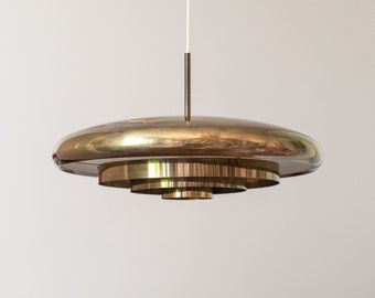 May include: A gold-toned, circular pendant light fixture with multiple tiers of concentric rings. The light fixture is suspended from the ceiling by a thin cord.