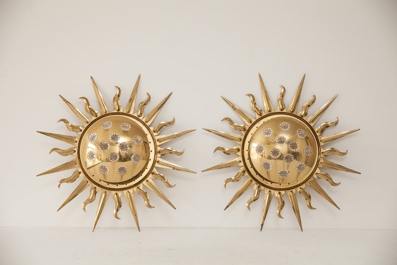 以下が含まれることがあります： 装飾的なテクスチャのある円形のセンターを持つ、ゴールドのサンバーストウォール sconces のペア。各 sconces は、16 本のポイントを持つスターバーストデザインです。