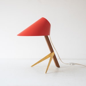 May include: A red and gold table lamp with a conical shade and a wooden base with three legs.