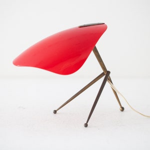 May include: A red table lamp with a triangular base and a curved shade. The lamp is made of metal and has a cord.