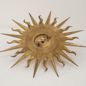 以下が含まれることがあります： 円形のセンターと尖った光線を持つ、金色の金属製のサンバーストウォールデコレーション。光線は波状のデザインになっています。