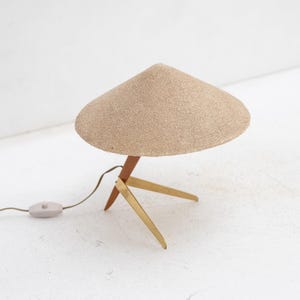 May include: A mid-century modern table lamp with a beige, conical shade. The lamp has a wooden stem and brass legs. The lamp has a cord with an on/off switch. The lamp is a decorative lighting fixture.