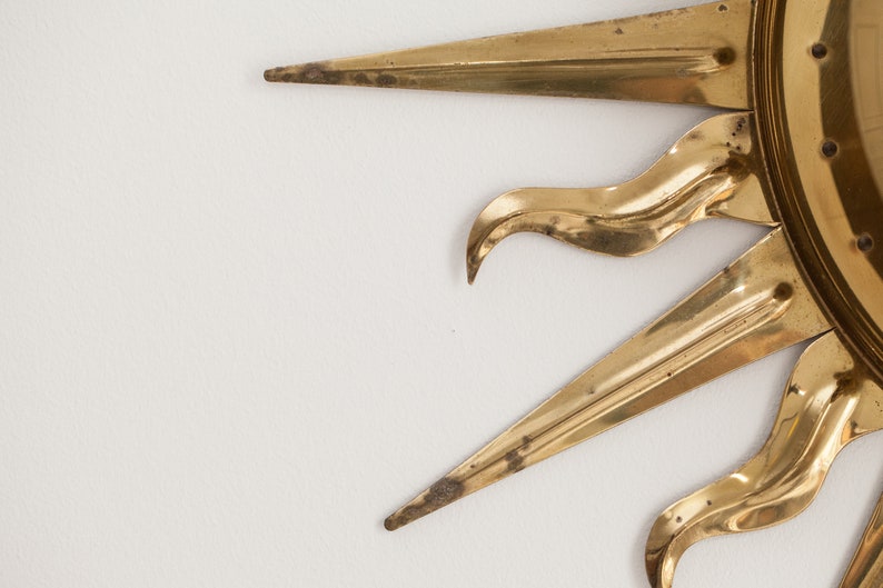 以下が含まれることがあります： 丸い中心と尖った光線を持つ金色のサンバーストミラー。ミラーは金属製で、ヴィンテージスタイルです。