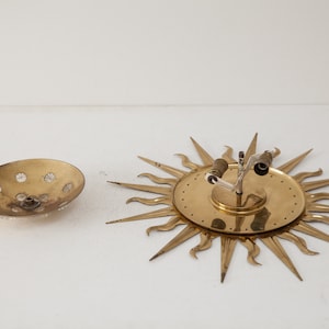 以下が含まれることがあります： 丸いテクスチャ加工されたガラス製のシェードが付いた、金色調のサンバーストウォール sconces。 sconces は、中心から放射状に伸びる尖った光線を持つ装飾的なデザインです。