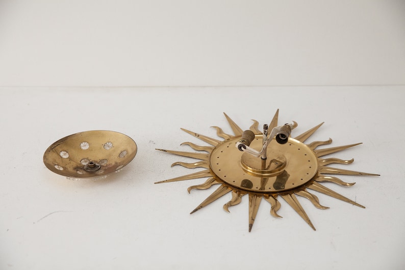 以下が含まれることがあります： 丸いテクスチャ加工されたガラス製のシェードが付いた、金色調のサンバーストウォール sconces。 sconces は、中心から放射状に伸びる尖った光線を持つ装飾的なデザインです。