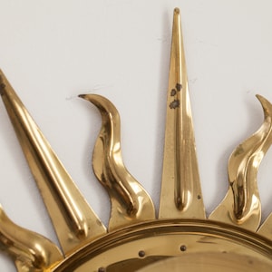 以下が含まれることがあります： 丸い中心と尖った光線を持つ、金色の金属製のサンバーストウォールデコレーションです。