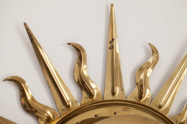 以下が含まれることがあります： 丸い中心と尖った光線を持つ、金色の金属製のサンバーストウォールデコレーションです。