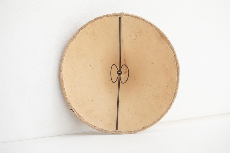 May include: A round, beige lampshade with a dark brown metal frame. The lampshade has a textured surface and a decorative metal element in the center. The lampshade is approximately 30 cm in diameter.