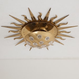 以下が含まれることがあります： クリスタルで覆われた丸いシェードが付いた、金色のサンバースト天井照明器具です。