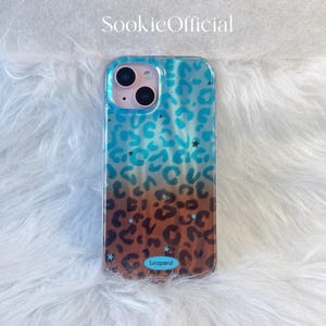 Può includere: Custodia trasparente per telefono con motivo leopardato. La custodia presenta una sfumatura di colori blu e marrone, con accenti di stelle nere. Il testo "Leopard" è stampato in basso.